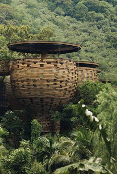 an unusual structure in the middle of some trees and bushes with mountains in the background