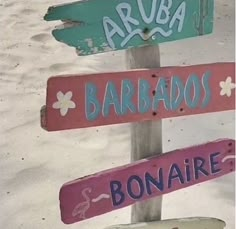 several wooden signs with different languages are on a pole in the sand at the beach