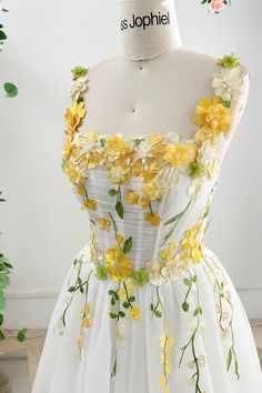 a white dress with yellow flowers and green leaves on the waistline is displayed in front of a mannequin