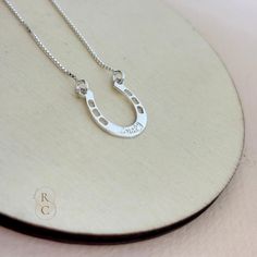 Add a touch of elegance and good luck to your jewelry collection with this custom Horseshoe Necklace. Crafted in high-quality sterling silver, this personalized necklace features a beautifully crafted horseshoe pendant, engraved with a word or name in an elegant font. The horseshoe is a timeless symbol of luck and protection. Wearing a horseshoe pendant is believed to bring good fortune and safeguard the wearer from negative energy. Our horseshoe pendant necklace makes a thoughtful and meaningfu Silver Necklaces With Hallmarks As Gift For Mom, Personalized Silver Jewelry For Good Luck, Personalized Silver Necklace For Good Luck, Horseshoe Shaped Sterling Silver Necklaces, Silver Horseshoe Jewelry Gift, Silver Sterling Silver Horseshoe Necklace, Sterling Silver Horseshoe Necklace For Gifts, Silver Horseshoe Necklace For Gift, Personalized Silver Horseshoe Jewelry