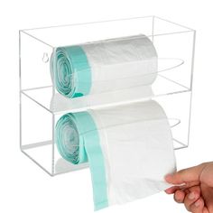 two rolls of toilet paper are being held by a person's hand in front of a clear acrylic holder