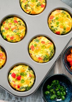 several muffins in a pan with different toppings next to bowls of vegetables