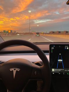 the dashboard of a vehicle with an electronic device on it's display screen, in front of a cityscape at sunset