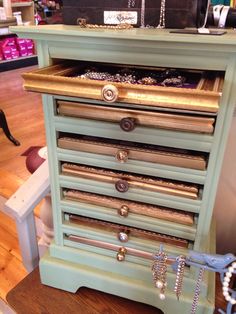 a green jewelry cabinet with many drawers and chains on the bottom shelf in a store