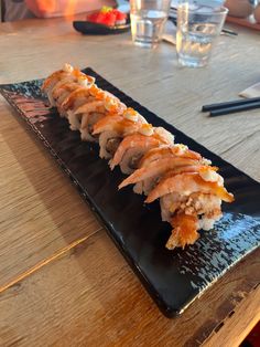 a black plate topped with sushi on top of a wooden table