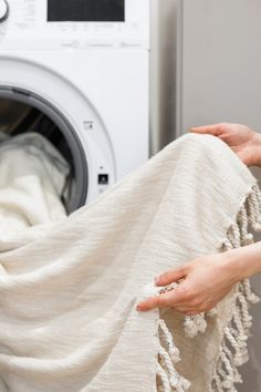 a woman is holding a blanket in front of a washer with her hands on it