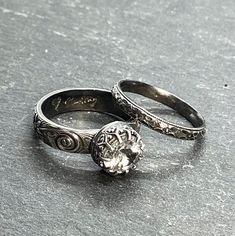 two wedding rings sitting next to each other on top of a gray surface with an intricate design