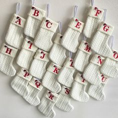 twelve pairs of white socks with red letters hanging from the hooks on a wall in a room