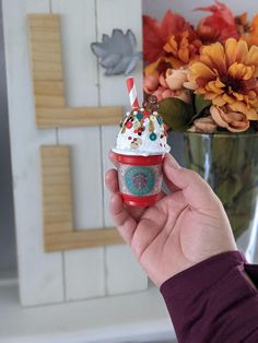 a hand holding an ice cream sundae with sprinkles on it in front of flowers