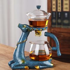 a glass coffee pot sitting on top of a wooden table next to a cup filled with liquid