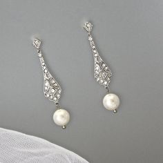 two pairs of pearl and diamond earrings on top of a white cloth covered tablecloth