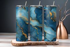 three blue and gold marbled tumbles sitting on top of a wooden stand next to a copper vase