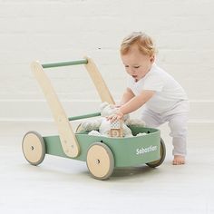 a baby playing with a green wagon filled with stuffed animals