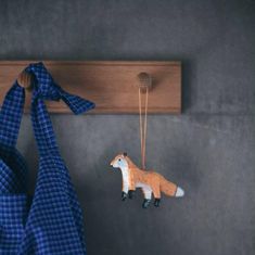 a toy fox hanging from a coat rack on the wall next to a blue scarf