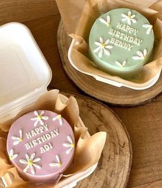 two decorated birthday cookies sitting on top of wooden trays next to an empty container