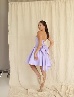 Introducing the Emily Dress with Bow: a stunning mini satin dress in a beautiful lilac color, designed to make you stand out. This dress features a dramatic maxi bow at the lower back, adding a bold and stylish touch that is perfect for girls who love to make a statement. The Emily Dress is not only eye-catching but also offers an impeccable fit with adjustable lacing at the back, ensuring you feel comfortable and confident throughout your special event. The elegant lilac hue enhances its sophis Open Back Dress With Bow, Short Dress With Bow In Back, Dress With A Bow On The Back, Dress With Big Bow On Back, Dresses With Bows In The Back, Dress With Bow In The Back, Bow Dresses Women, Bow Dress Outfit, Short Dress With Bow