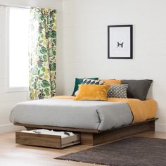 a bed with yellow and gray pillows in a room next to a window, rugs and curtains