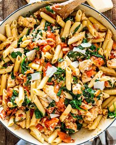 pasta with chicken, spinach and tomato sauce in a skillet on a wooden table