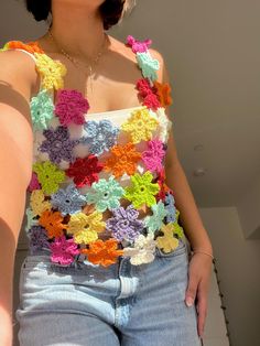 a woman wearing shorts and a top with crocheted flowers on the bottom, standing in front of a wall