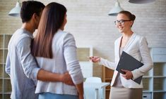 two women are talking to each other in an office with hanging lights and she is holding a binder