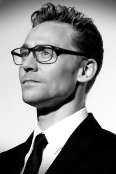 a man wearing glasses and a suit looks off into the distance