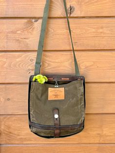 a green bag hanging on the side of a wooden wall with a flower in it