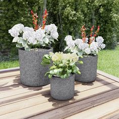 three cement planters with flowers in them on a wooden table outside near some trees