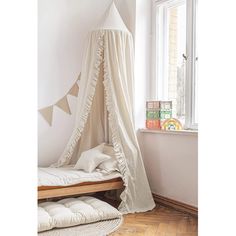 a white canopy bed in a bedroom next to a window with bunting curtains on it