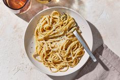 a white plate topped with pasta next to a glass of wine