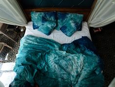 a bed with blue and green pillows on top of it next to white drapes