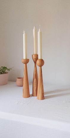 three wooden candlesticks sitting on top of a white table cloth next to a potted plant