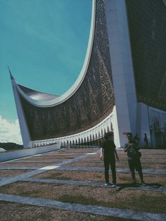 two people standing in front of a large building with an intricate design on it's side