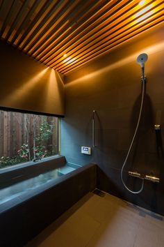 a bathroom with a large window and wooden slats on the ceiling, along with a shower head