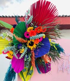 a bouquet of colorful flowers and palm leaves in front of a happy birthday sign