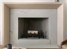 a living room with a fire place and two chairs in front of the fireplace that is white marble