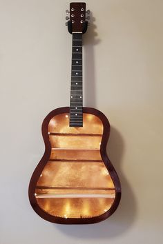 an acoustic guitar hanging from the wall with lights on it's back and sides