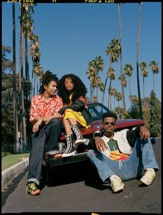 three people sitting on the back of a car in front of palm trees and blue sky