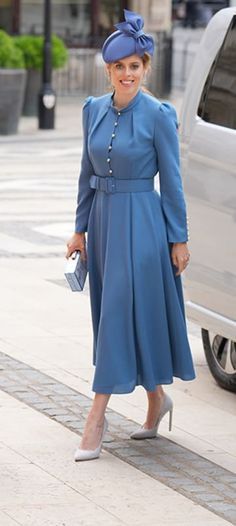 a woman in a blue dress and hat standing next to a car