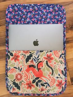 an open laptop computer sitting on top of a flower covered bag with the cover closed