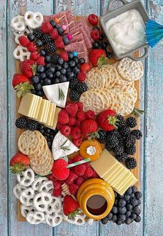 an assortment of cheeses, crackers, berries and pretzels on a wooden board