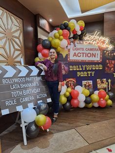 a woman standing in front of a hollywood sign with balloons and signs around it that read, lights camera action