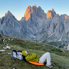 a man laying on top of a lush green field next to mountains covered in snow