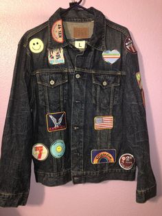 a denim jacket with patches on it hanging from a hook in a pink walled room