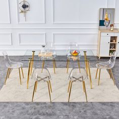 a glass dining table with gold legs and clear chairs in front of a white wall