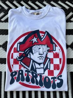 Get this popular new Patriots Mascot shirt and show off your school spirit in style!  Each shirt is printed in-house by me using high-quality materials on a Comfort Colors shirt, known for its exceptional comfort, style, and durability. Shown in Natural. Even the glitter is printed! No need to worry about peeling glitter vinyl, or messy glitter flakes. Available in unisex sizes S to 3X, and youth sizes, we've got you covered regardless of your preferred fit. The Preppy Patriots Shirt features a classic crew neck and short sleeves, making it suitable for year-round wear. The flattering silhouette ensures a comfortable and stylish fit for both men and women. Please note that ivory is ONLY available in Adult sizes!  Note: As each shirt is individually printed, slight variations in color and p Patriot School Spirit Shirts, Patriots School Spirit Shirts, Cheap White School Spirit Shirt, School Spirit Graphic T-shirt Fan Gear, School Spirit Graphic T-shirt For Fan Gear, School Spirit Graphic Print T-shirt For Fan Gear, School Spirit Graphic T-shirt, Graphic Print Cotton Shirt For College, Custom Print Sports Fan T-shirt