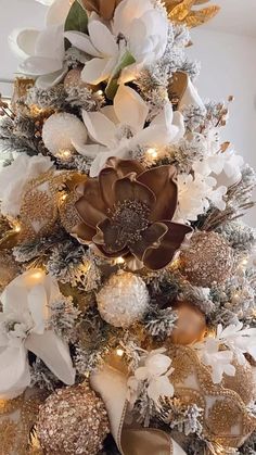 a christmas tree decorated with gold and white flowers, silver ornaments and golden ribbon bows