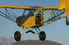 a small yellow airplane flying over a mountain