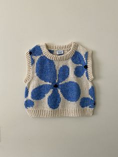 a blue and white flower sweater hanging on a wall next to a small stuffed animal