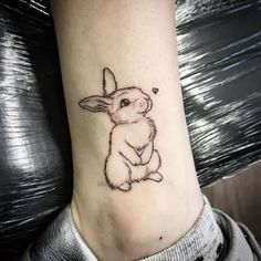 a small rabbit tattoo on the ankle is shown in black and grey ink, with an outline of a bunny sitting next to it's head