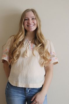 This cream top features an embroidered design on the neckline and sleeves, with tassel strings. This top is running oversized. Model is wearing a size SMALL. Model is 5 ft. 3 in. - 125ish lbs. Model typically wears small/medium in tops. Bohemian Cotton Blouse With Fringe, Beige Floral Embroidery Tops For Festival, Casual Cotton Blouse With Tassel Ties, Casual Festival Tops With Tassels, Casual Tops With Tassels For Festival, Bohemian Cotton Top With Tassel Ties, Bohemian Cotton Tops With Tassel Ties, Bohemian Short Sleeve Blouse With Tassels, Spring Blouse With Tassel Ties And Short Sleeves